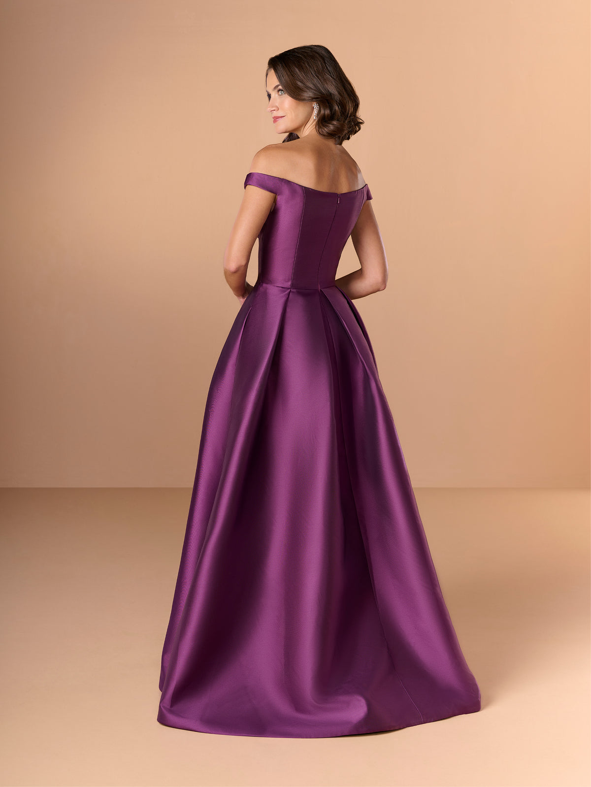Woman wearing a purple off-shoulder gown against a beige background / Off the shoulder gown with side skirt panels and inserted neckline beading.