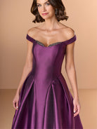 Woman wearing a purple off-shoulder gown with beaded details on a beige background / Off the shoulder gown with side skirt panels and inserted neckline beading.
