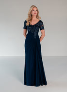 A woman modeling a floor-length navy evening gown with a beaded lace bodice, short sleeves, and a draped skirt, photographed against a neutral light gray studio background. / Slim A-line style with chiffon skirt and beaded lace bodice, V-neck with short sleeves and side front draping on skirt.