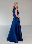 A woman modeling a floor-length royal blue satin gown with a sleeveless V-neckline and structured back, photographed in a clean studio setting. / A-line mikado style with V-neck and short cup sleeves. Side front draping on bodice finished with ruffle on side front skirt.