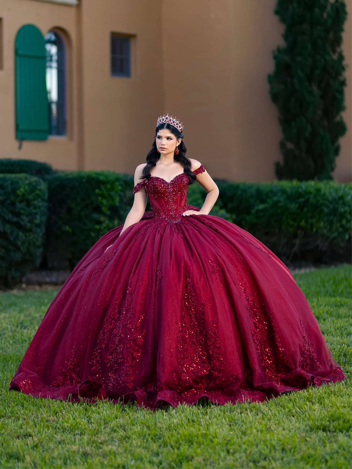 This ball gown features a richly embroidered bodice with off-the-shoulder straps. The full, voluminous skirt is decorated with shimmering floral detailing and flows into an elegant train accented with a bow at the back.