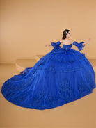 This ball gown features a fitted, embroidered bodice with off-the-shoulder sleeves. The full layered skirt includes cascading floral details and is finished with a dramatic bow and long, flowing train.
