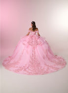 A woman viewed from behind wearing an elaborate off-the-shoulder pink ball gown with a large bow at the back and a long train covered in floral lace and beadwork, set against a soft pink studio background. / Stunning off-shoulder ball gown with shimmering embellished appliqués, a structured corset bodice, a full tulle skirt, and a dramatic oversized bow with a sweeping train.