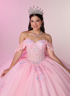 A young woman wearing a sparkling off-the-shoulder pink quinceañera ball gown with blue floral embroidery, a silver tiara, and a matching silver necklace, posed against a soft pink studio backdrop. / Romantic off-shoulder ball gown with delicate embellished appliqués, a fitted bodice, a voluminous tulle skirt, and a statement bow at the back.