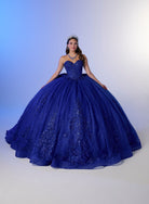 A woman wearing a voluminous royal blue ball gown with lace detailing and a tiara, posed against a blue-to-white studio backdrop. / Elegant off-shoulder ball gown adorned with intricate sparkling appliqués, a structured sweetheart bodice, a voluminous skirt, and a dramatic oversized bow with a sweeping train.