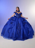 A woman wearing a voluminous royal blue off-the-shoulder ball gown with intricate lace and sequin embellishments, posed against a soft blue-to-white studio backdrop. / Elegant off-shoulder ball gown featuring sparkling embellished appliqués, a structured corset bodice, dramatic layered skirt details, and a voluminous princess silhouette.