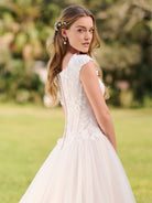 Woman in a white lace dress standing outdoors with greenery in the background / Cap sleeve Basque waist tulle ballgown with corsetry lines and 3D flower lace appliques.