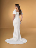 Woman wearing a white wedding dress with a plain background / Slim crepe dress with square neckline and puffy short sleeves. Buttons at the back along zipper closure and all the way down on train.