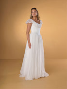 Woman wearing a white dress against a beige background / A-line gown in crinkled organza and satin midriff area on bodice only. Short puffy sleeves. Covered buttons along zipper closure at the back dress.