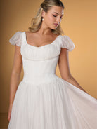Woman wearing a white dress with puffed sleeves against a beige background / A-line gown in crinkled organza and satin midriff area on bodice only. Short puffy sleeves. Covered buttons along zipper closure at the back dress.