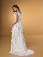 Woman wearing a white wedding dress with ruffled details on a beige background / Slim A-line style in charmeuse with ruffles decorating V-neck and skirt.