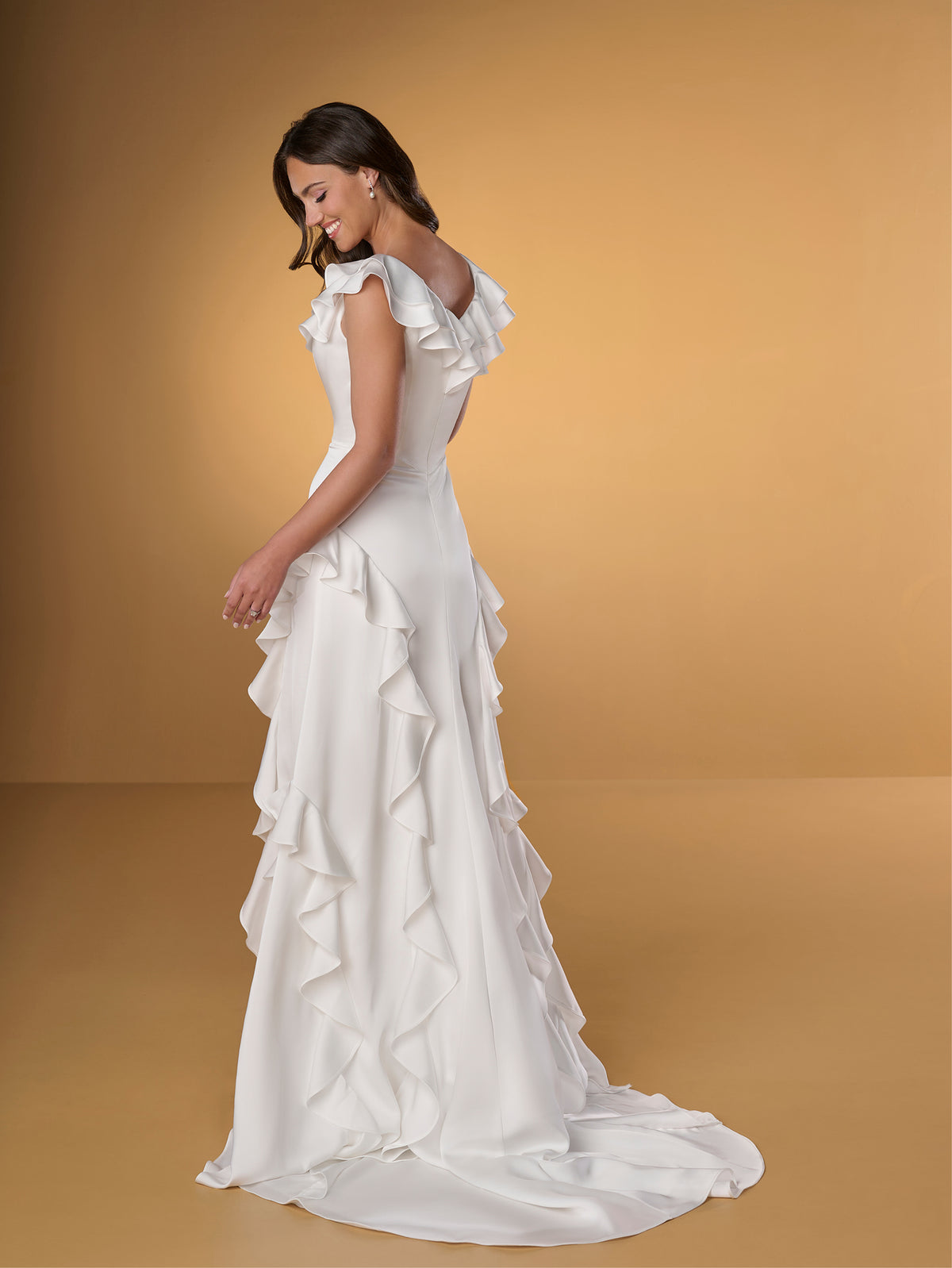 Woman wearing a white wedding dress with ruffled details on a beige background / Slim A-line style in charmeuse with ruffles decorating V-neck and skirt.
