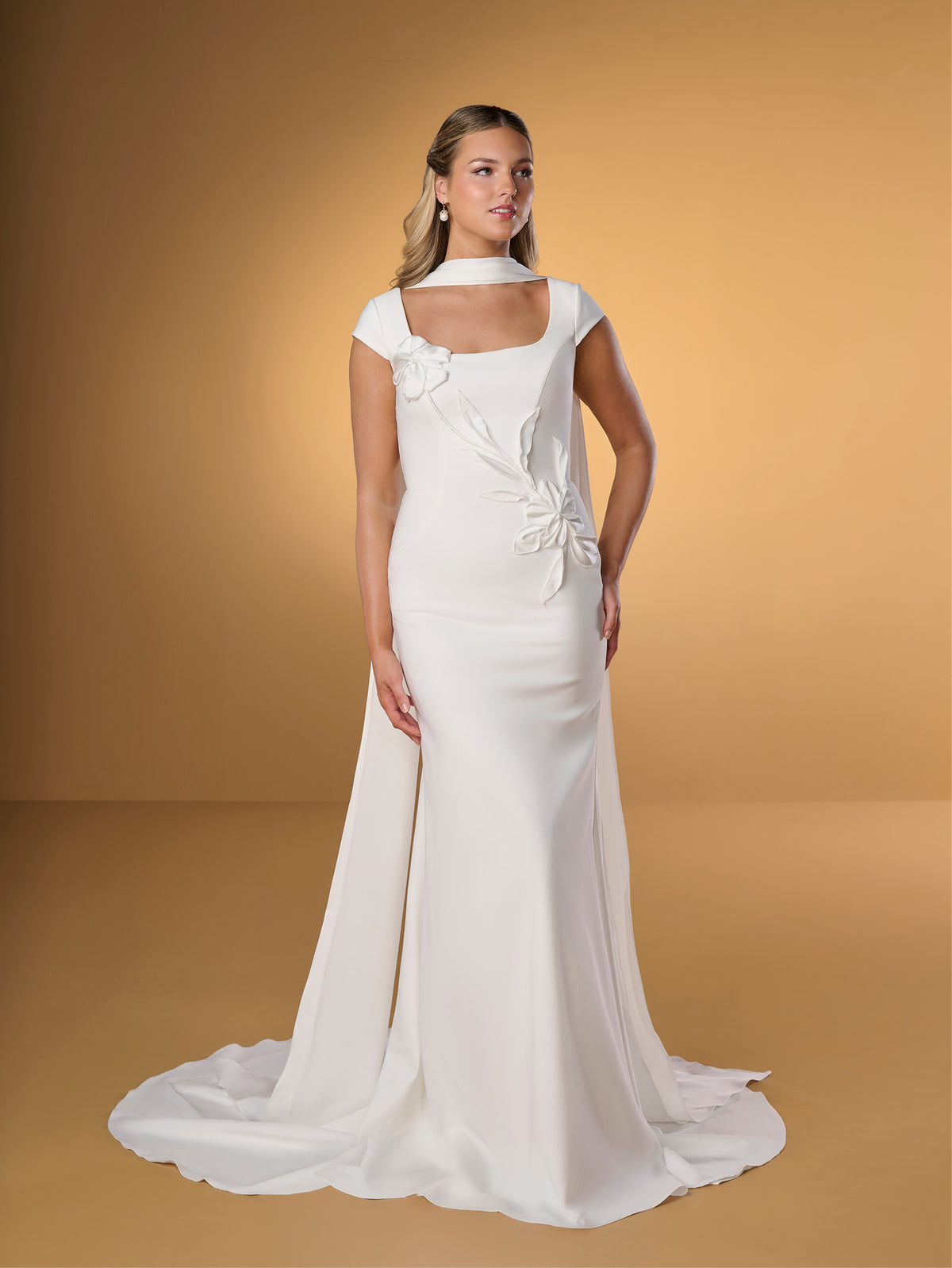 Woman wearing a white wedding dress against a beige background / Slim crepe style with square neckline and cup sleeves, decorated with 3D motifs in soft crinkle organza fabric. Covered buttons along zipper closure at the back.