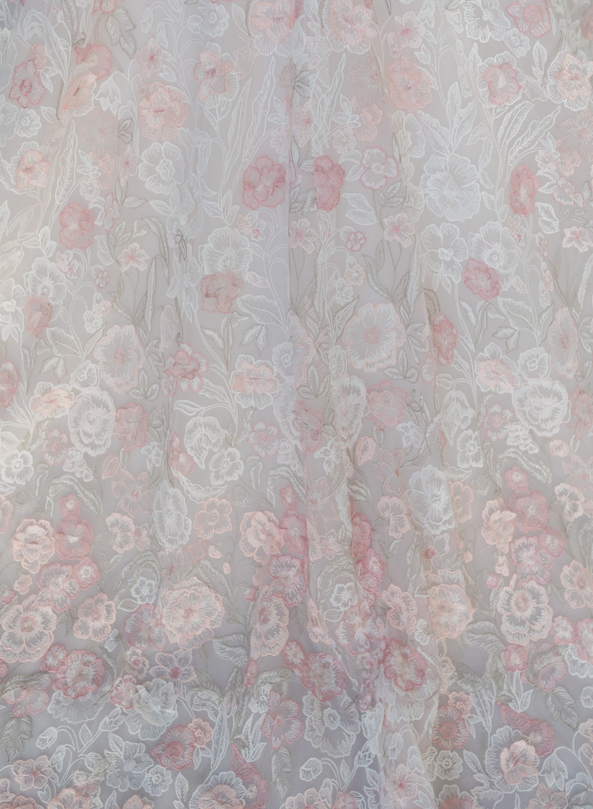 A close-up of a sheer floral fabric with a delicate pattern of pink, dusty rose, and white flowers on a light gray base. / All over multicolored lace A-line gown.