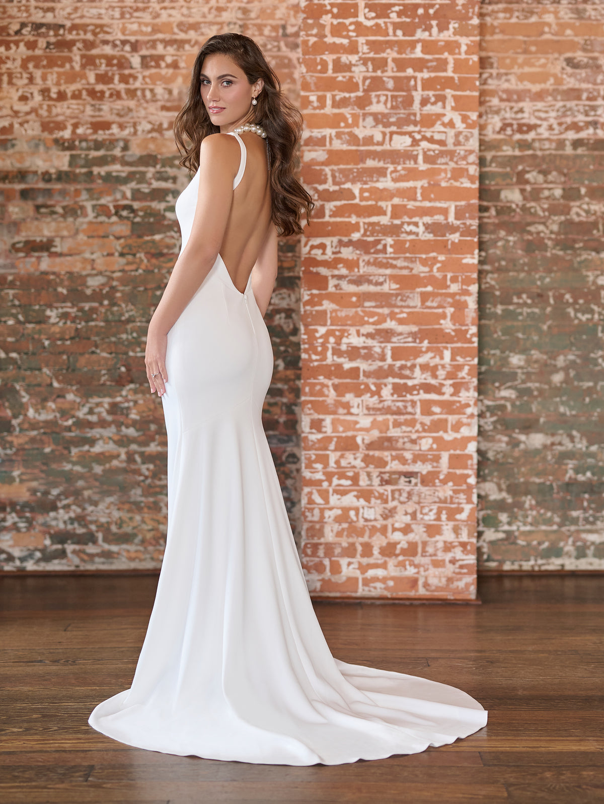 Woman in a white wedding dress with a brick wall background / This stretch crepe gown has a plunging front neckline and a low, sexy back.
