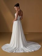 A woman modeling a strapless white wedding gown with a fitted lace bodice and a long flowing train, photographed in a warm brown studio setting. / Faux 2-piece gown with lace bodice and full skirt.