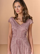 A woman wearing a dusty rose lace dress with cap sleeves and a V-neckline, standing against a solid beige background. / All over beaded gown with sheer cap sleeve, v neckline and full, A-line skirt.