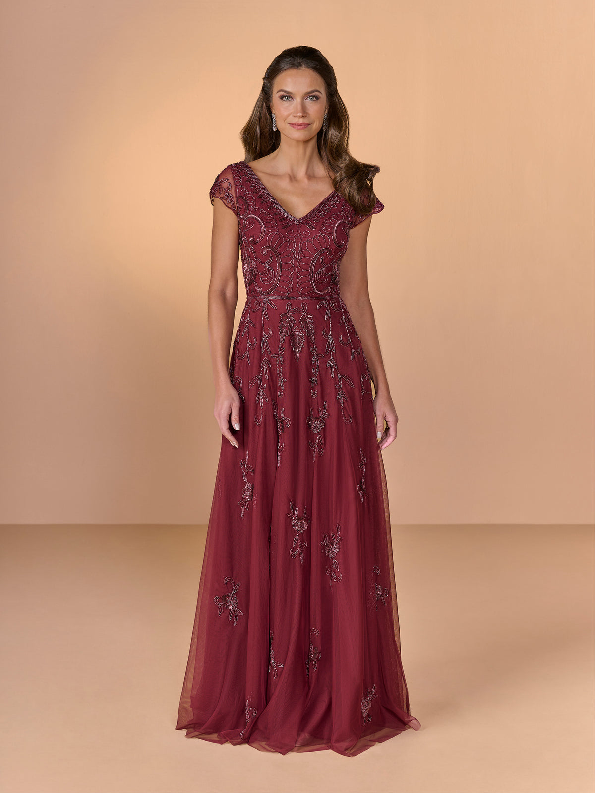 Woman wearing a burgundy evening gown with lace details on a beige background / All over beaded gown with sheer cap sleeve, v neckline and full, A-line skirt.