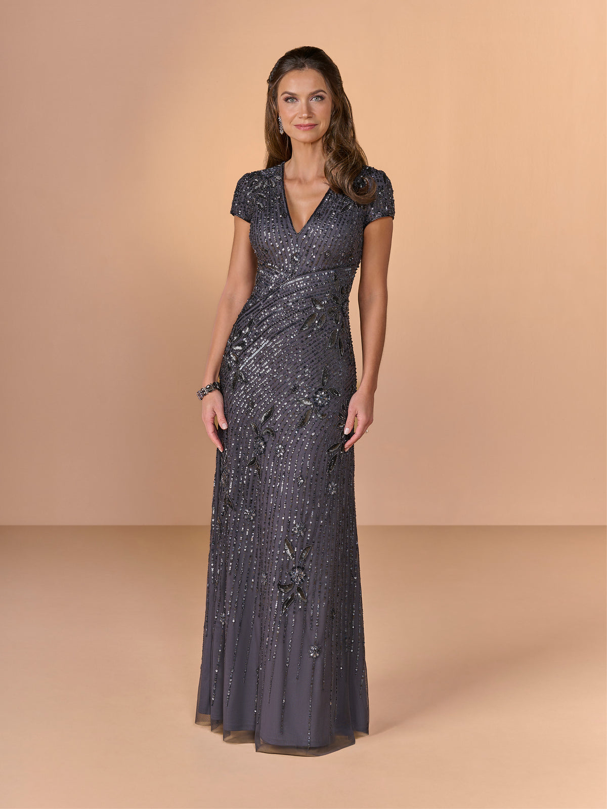 Woman wearing a dark gray evening gown with a V-neckline on a beige background / All over beaded gown with v neckline and cap sleeve.