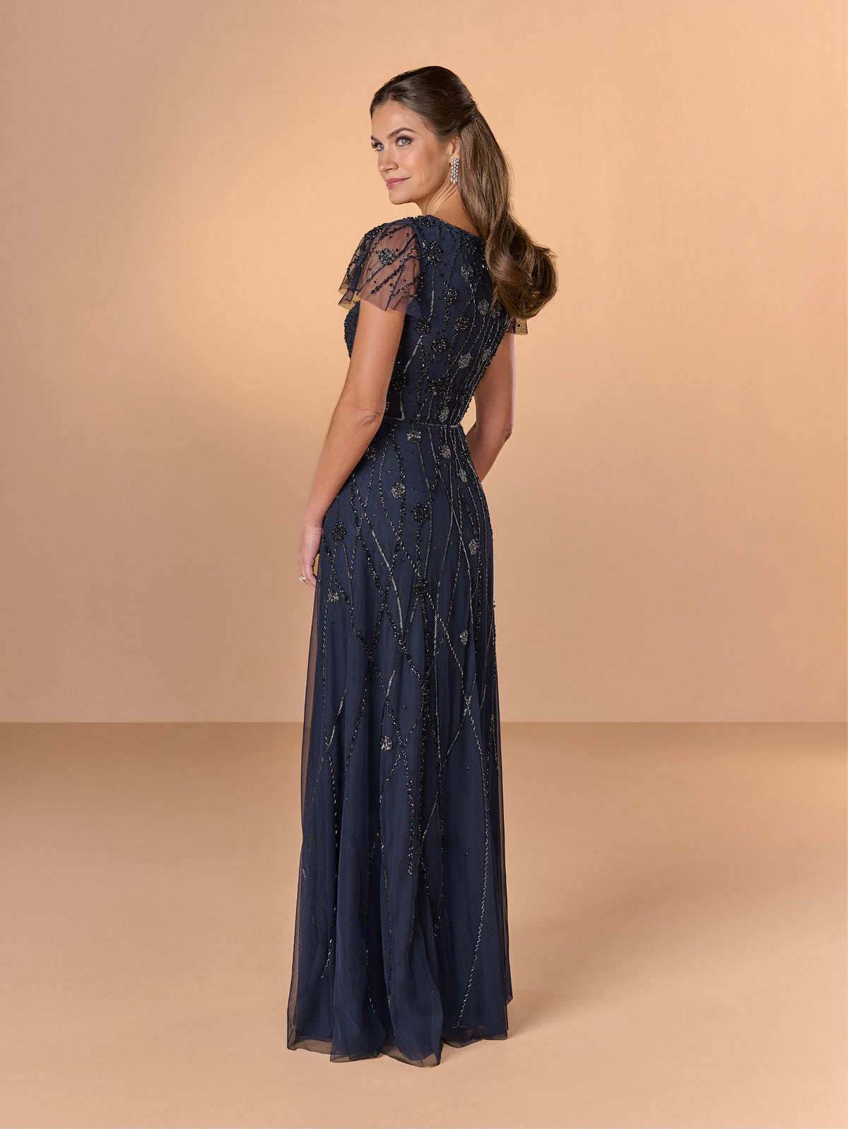Woman wearing a navy blue lace evening gown against a beige background / All over beaded gown with v neckline and soft A-line skirt.