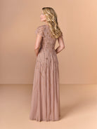 A woman wearing a floor-length dusty rose formal gown with intricate beadwork and sequin embellishments, shown from the back against a solid beige studio backdrop. / All over beaded gown with v neckline and soft A-line skirt.