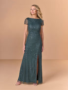 A woman modeling a floor-length, dark teal sequined gown with sheer cap sleeves and a high front slit, posed against a solid warm beige studio backdrop. / All over beaded gown with body shirring, skirt slit and back cowl detail.