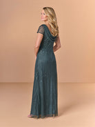 Woman wearing a long, dark green dress with sequin details on a beige background / All over beaded gown with body shirring, skirt slit and back cowl detail.