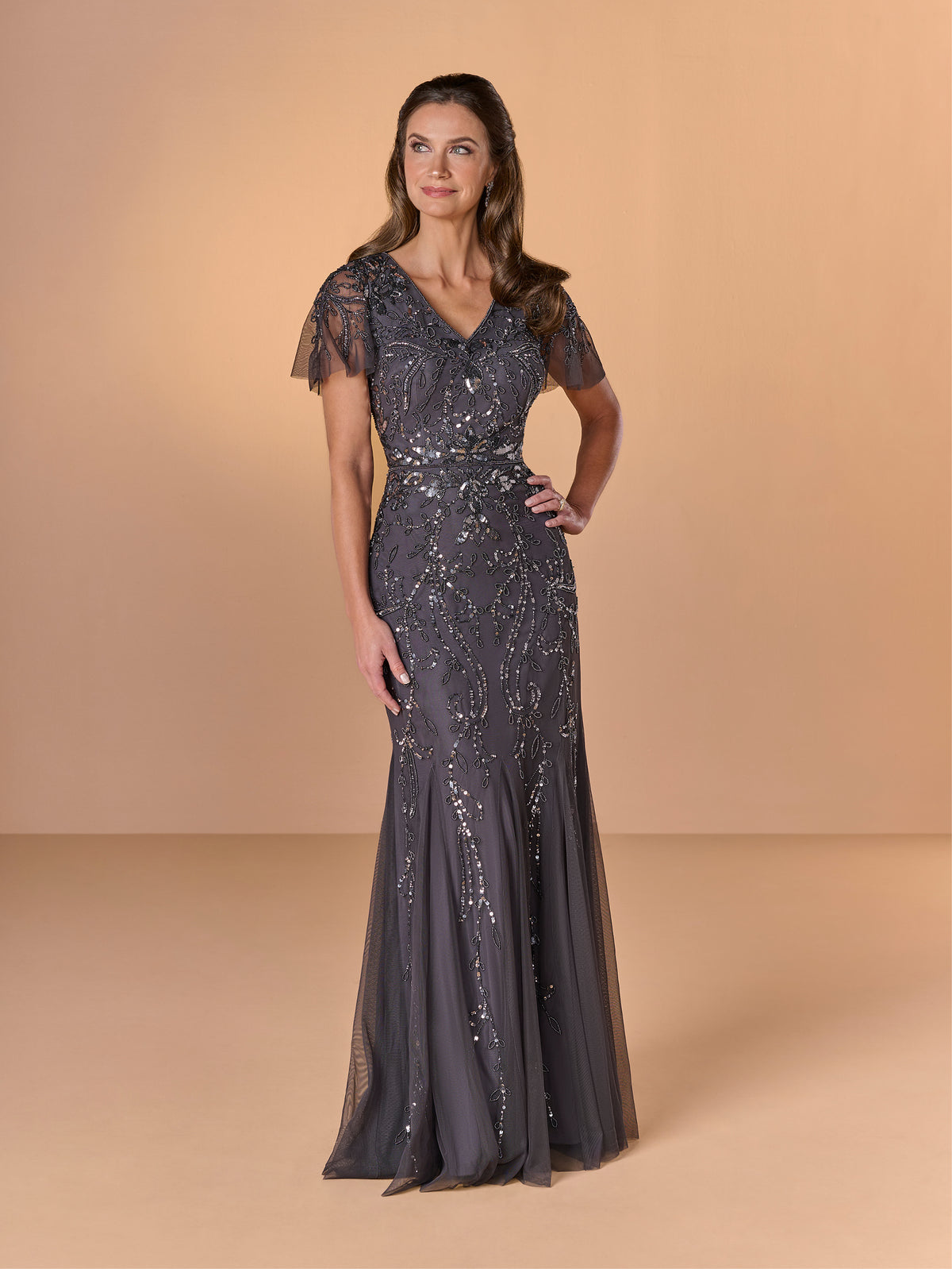 Woman wearing a dark gray evening gown with lace details on a beige background / All over beaded gown with short flutter sleeve and soft godet skirt.
