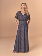 Woman wearing a dark gray evening gown with lace sleeves on a beige background / All over beaded gown with surplice, blouson bodice and soft A-line skirt.