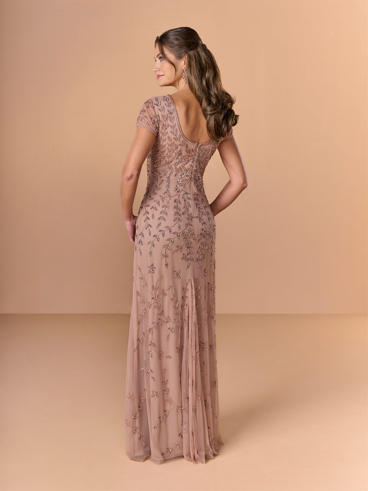 Woman wearing a long, elegant dress with floral patterns on a beige background / All over beaded gown with scoop neck and short sleeve.