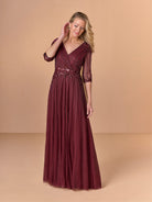 Woman wearing a burgundy evening gown with a beige background / All over beaded gown with surplice bodice, elbow length sleeve and full A-line skirt.