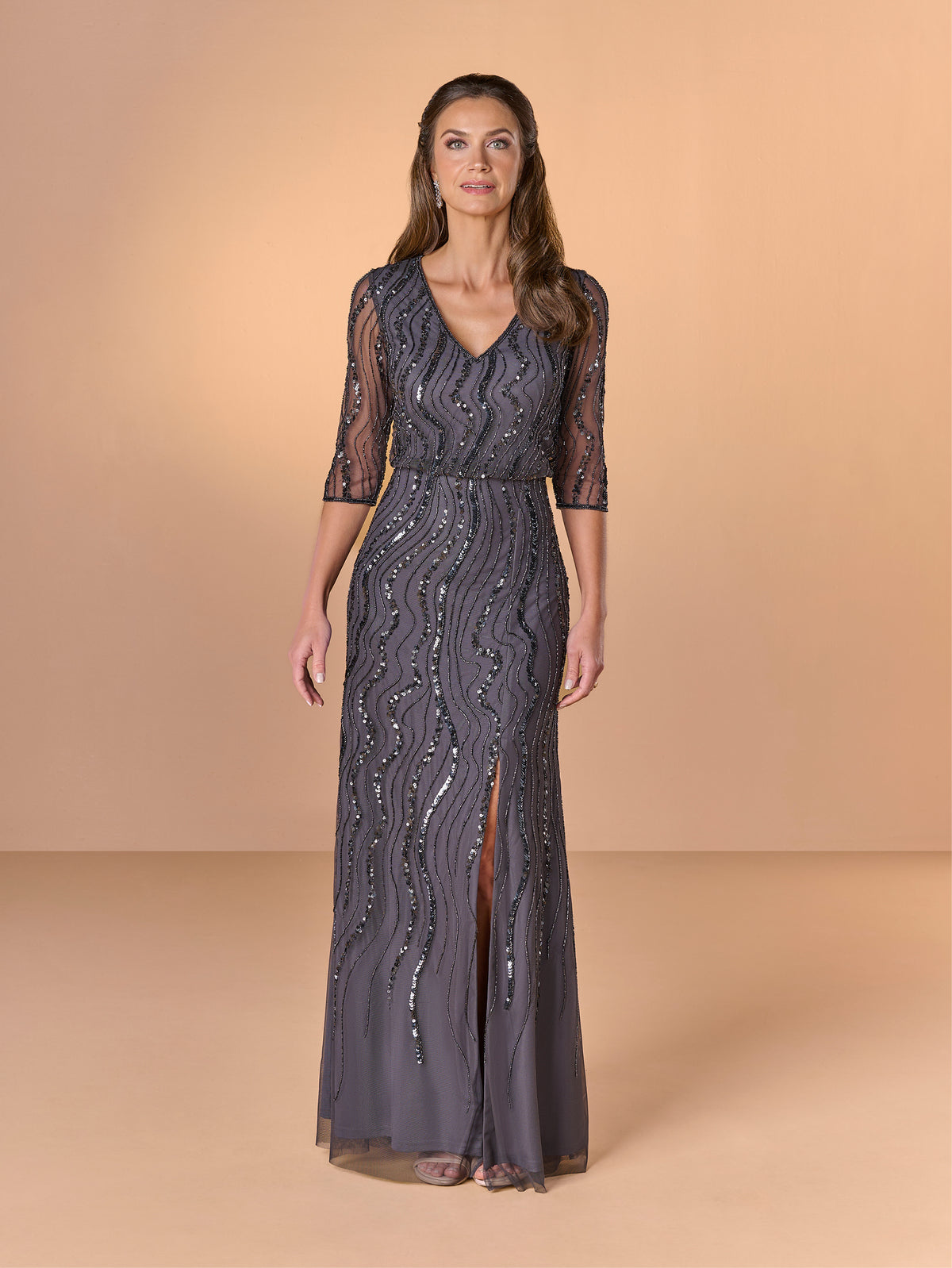 Woman wearing a dark gray lace evening gown with a V-neck and quarter sleeves on a beige background / All over beaded gown with v neckline, blouson bodice and slim slit skirt.