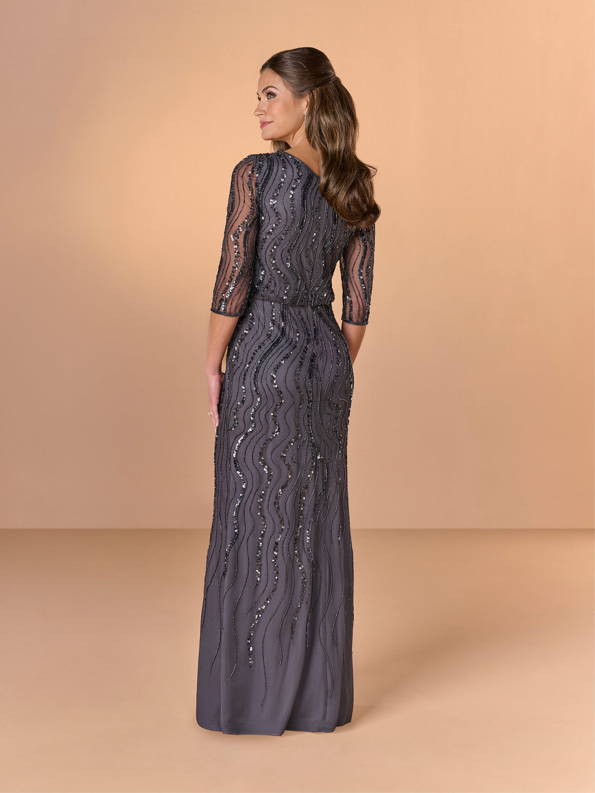 Woman wearing a dark gray lace dress against a beige background / All over beaded gown with v neckline, blouson bodice and slim slit skirt.