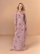 A woman models a floor-length dusty rose formal gown with floral sequin embroidery, paired with a matching sheer shrug, against a solid beige studio backdrop. / All over beaded gown with high straight neckline, 3D flowers and matching separate shawl.