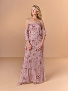A woman models a strapless dusty rose tulle gown with floral sequin and bead embroidery, styled with a matching draped shawl, set against a solid beige studio backdrop. / All over beaded gown with high straight neckline, 3D flowers and matching separate shawl.