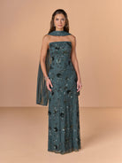 Woman wearing a dark green strapless gown with floral patterns on a beige background / All over beaded gown with high straight neckline, 3D flowers and matching separate shawl.