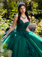 A woman wearing an emerald green quinceañera dress with a sweetheart bodice, beaded embellishments, and a voluminous tulle skirt, posed outdoors in a garden setting with a matching tiara and necklace. / This ball gown features a floral-embellished bodice and a full tulle skirt with cascading 3D flowers, finished with a decorative bow at the back.