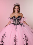A smiling young woman wearing a voluminous pink ball gown with a black lace corset bodice, off-the-shoulder ruffled sleeves, and a matching pink tiara against a soft pink studio background. / A strapless ball gown with a lace-up bodice and a voluminous tulle skirt featuring floral embroidery and a large back bow.