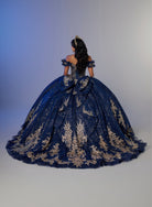 A woman photographed from behind wearing an elaborate royal blue ball gown with extensive gold floral embroidery, set against a neutral studio background. / An off-the-shoulder ball gown with ruffled cap sleeves, a heavily embroidered metallic bodice, and a voluminous glitter-tulle skirt adorned with intricate baroque-style appliques and a matching oversized back bow.