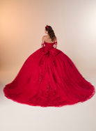 A woman viewed from behind wearing an elaborate off-the-shoulder red ball gown with a very full skirt, large bow at the back, and embroidered detailing, standing against a warm beige studio backdrop. / Ball gown with a lace-detailed back, corset lacing, and a large bow at the waist. The full skirt has a subtle sparkle and elegant embroidery.