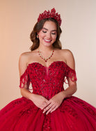 A smiling young woman wearing a bright red off-the-shoulder quinceañera dress with heavy beadwork, a matching red tiara, and a red beaded necklace, posed against a warm beige studio background. / Ball gown with a lace-detailed back, corset lacing, and a large bow at the waist. The full skirt has a subtle sparkle and elegant embroidery.