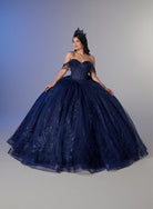 A woman wearing a voluminous navy blue ball gown with floral lace detailing and a matching tiara, posed against a neutral gray studio background. / Ball gown with a lace-detailed back, corset lacing, and a large bow at the waist. The full skirt has a subtle sparkle and elegant embroidery.