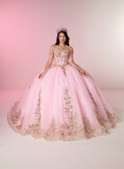 A woman wearing a voluminous light pink ball gown with gold floral embroidery and a matching tiara, posed against a soft pink studio backdrop. / Two-piece off-shoulder dress with a fitted, embellished bodice and a short, form-fitting skirt, featuring a sweetheart neckline, sparkling embroidered details, detachable arm drapes, and a full tulle skirt with a sweeping train.