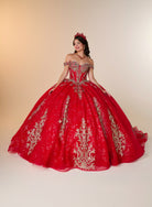 A woman modeling a voluminous red quinceañera ball gown with intricate gold embroidery and off-the-shoulder straps, set against a plain beige studio background. / Elegant off-shoulder ball gown featuring intricate embroidered detailing, a structured bodice, and a voluminous skirt with a dramatic statement bow at the back.