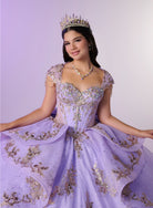 A young woman wearing an elaborate lavender quinceañera dress with gold sequin embroidery, a matching tiara, and a necklace, posing against a light purple studio background. / Regal ball gown featuring intricate embroidered appliqués, a structured bodice, dramatic layered overskirt details, and a sweeping cathedral-length train for a royal-inspired look.