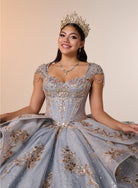 A woman wearing an ornate light blue ball gown with gold embroidery, a matching tiara, and a necklace, posing against a solid beige background. / Regal ball gown featuring intricate embroidered appliqués, a structured bodice, dramatic layered overskirt details, and a sweeping cathedral-length train for a royal-inspired look.