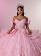 A young woman wearing a voluminous pink ball gown with off-the-shoulder straps, a jeweled corset bodice, and a sparkling tiara, posed against a soft pink studio background. / Princess-inspired ball gown featuring a sweetheart corset bodice, intricate floral appliqués, dramatic layered overskirt details, and a voluminous skirt with a statement bow at the back.