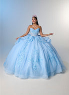 A woman wearing a voluminous light blue ball gown with floral lace appliqué and a sweetheart neckline, posed against a soft blue-to-white studio backdrop. She is wearing a small tiara and necklace. / Princess-inspired ball gown featuring a sweetheart corset bodice, intricate floral appliqués, dramatic layered overskirt details, and a voluminous skirt with a statement bow at the back.
