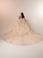 A woman stands with her back to the camera wearing an elaborate off-white ball gown with a very long train, decorated with pastel blue and lavender floral embroidery and beadwork, set against a plain light beige studio background. / Enchanting ball gown featuring a structured sweetheart corset bodice, shimmering embroidered details, dramatic layered ruffles, and a sweeping cathedral-length train for a regal princess-inspired look.