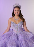 A smiling young woman wearing a sparkling lavender quinceañera-style gown with a fitted embellished bodice and voluminous tulle skirt, along with a jeweled tiara and matching necklace, posed against a soft lavender studio background. / Enchanting ball gown featuring a structured sweetheart corset bodice, shimmering embroidered details, dramatic layered ruffles, and a sweeping cathedral-length train for a regal princess-inspired look.